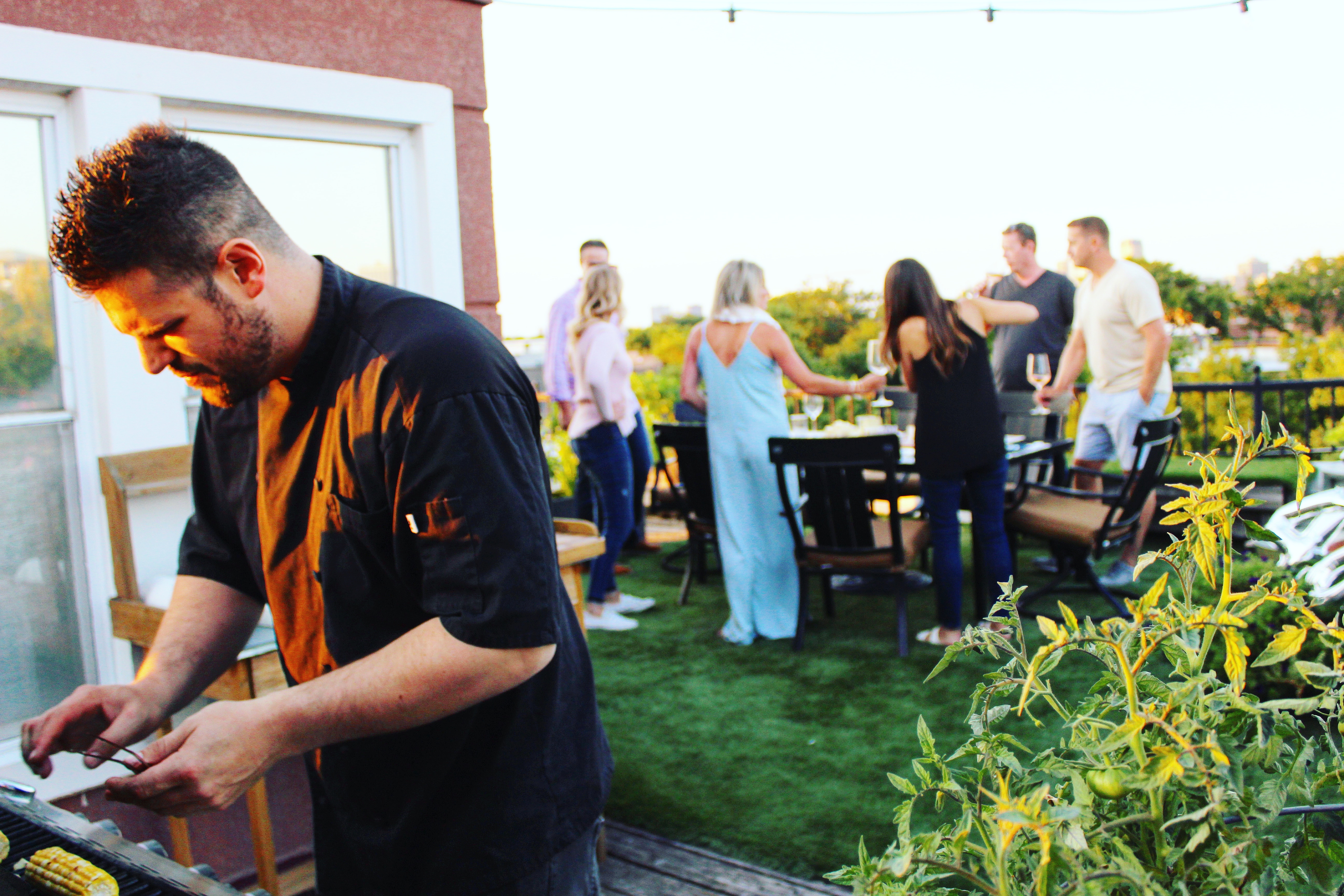 Chef Frank grilling at a rooftop dinner party with guests socializing